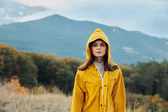 Молодая женщина в жёлтом дождевике на фоне осенних гор