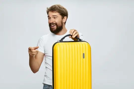 Бородатый мужчина с жёлтым чемоданом радостно указывает в сторону