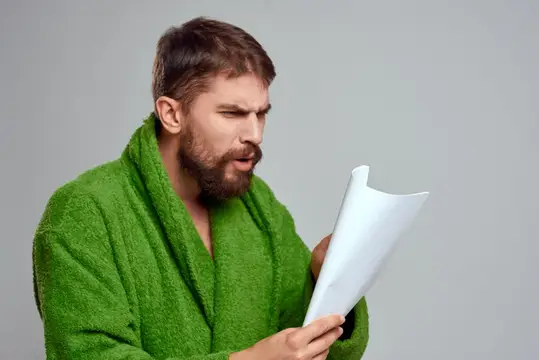 Бородатый мужчина в зелёном халате удивлённо читает документ