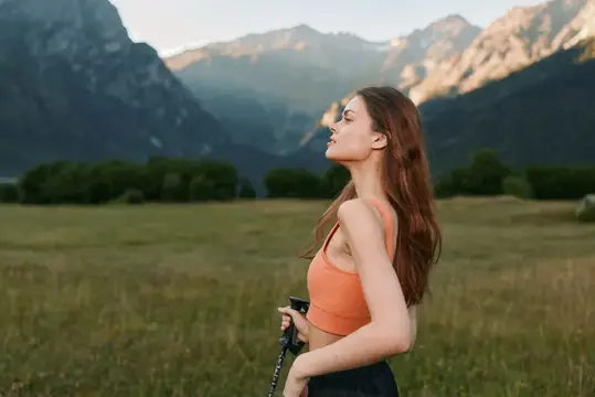 Девушка с треккинговой палкой отдыхает на лугу в горах
