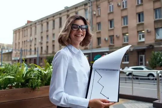 Улыбающаяся женщина в очках с папкой документов на городской улице
