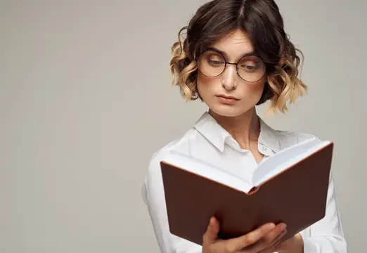 Умная женщина с блокнотом в руках, одетая в белую рубашку, на сером фоне, крупный план