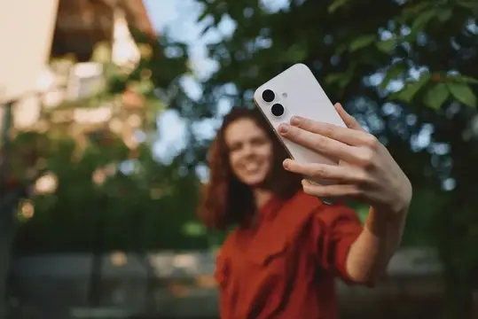 Улыбающаяся девушка делает селфи на смартфон на улице
