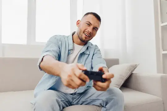 Улыбающийся мужчина играет в видеоигру с геймпадом на диване