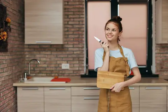 Улыбающаяся девушка в фартуке с ножом на кухне