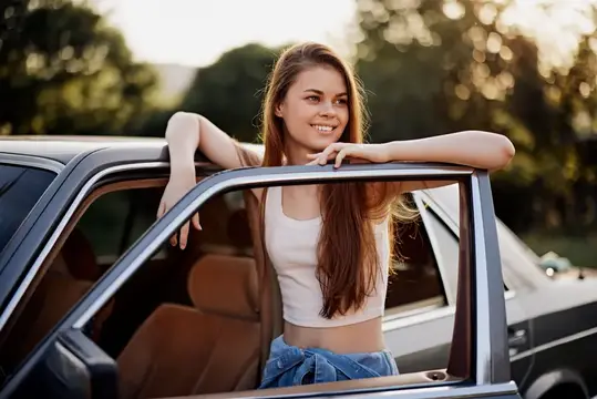 Улыбающаяся девушка с длинными волосами выглядывает из окна автомобиля