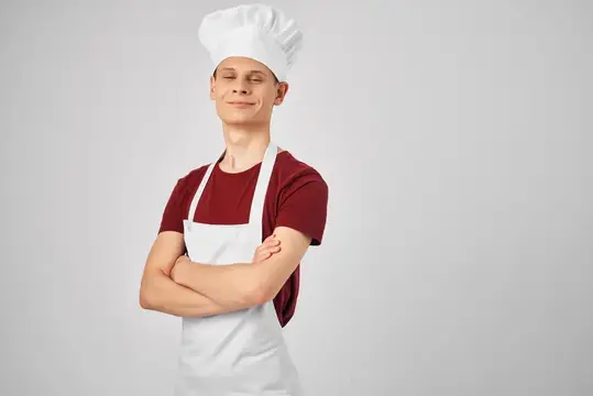 Молодой повар в колпаке и фартуке стоит со скрещёнными руками