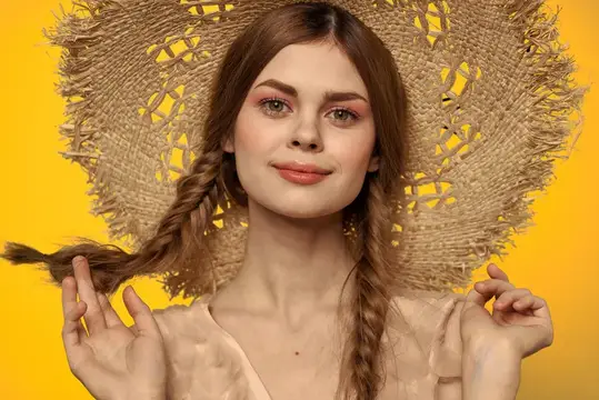 Молодая женщина с косами в соломенной шляпе на жёлтом фоне