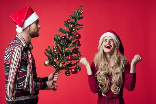 Мужчина с бородой дарит смеющейся блондинке украшенную ёлку на красном фоне