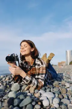 Молодая женщина лежит на галечном пляже с фотокамерой