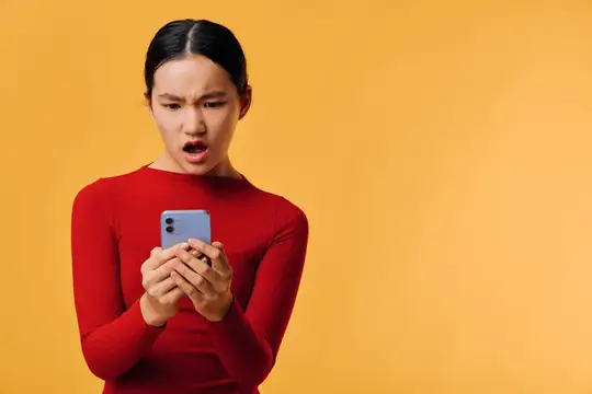 Женщина держит телефон с интенсивным удивленным выражением лица на желтом фоне
