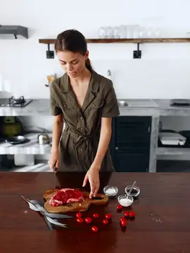 Молодая женщина нарезает мясо на кухонной доске
