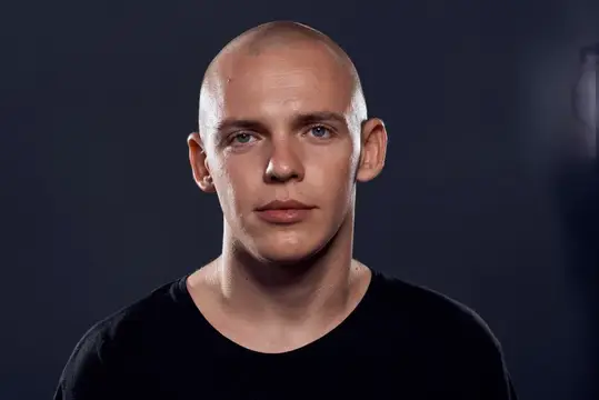 Портрет молодого лысого мужчины в чёрной футболке на тёмном фоне