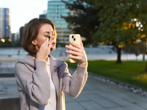 Веселая женщина пользуется смартфоном в городском парке, запечатлевая момент самовыражения