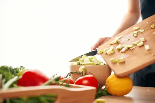 Повар нарезает овощи на доске среди свежих продуктов
