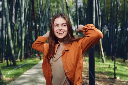 Улыбающаяся девушка в оранжевой куртке гуляет по бамбуковой роще