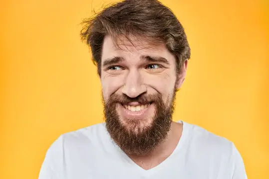 Улыбчивый бородатый мужчина в белой футболке на жёлтом фоне