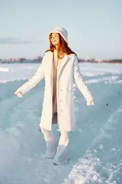 Женщина улыбается, прогуливаясь в белом пальто, наслаждаясь зимним настроением и свежим воздухом