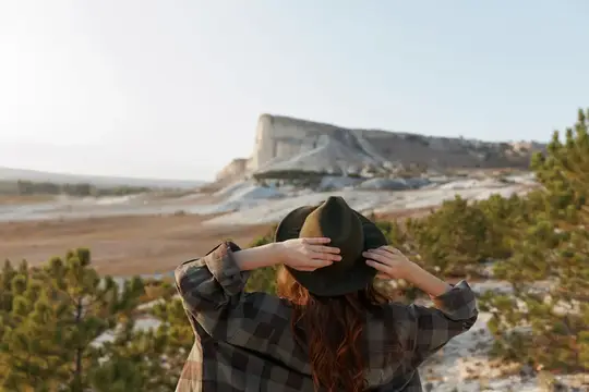 Девушка в клетчатой рубашке и шляпе смотрит на белую скалу