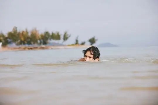 Мальчик с мокрыми волосами купается в море на фоне берега