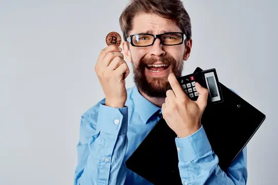 Бородатый мужчина в очках с монетой биткоина и калькулятором