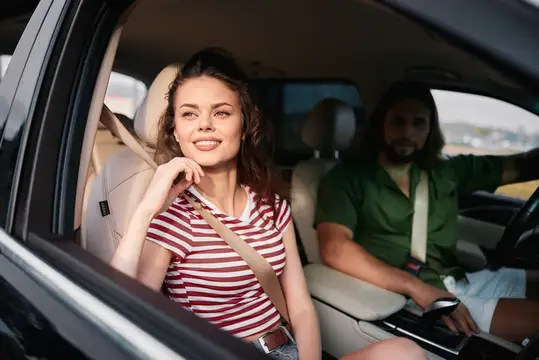 Улыбающаяся девушка на пассажирском сиденье автомобиля с мужчиной за рулём