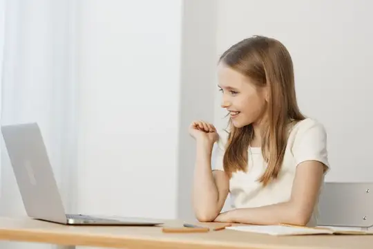 Улыбающаяся девочка смотрит в ноутбук за столом