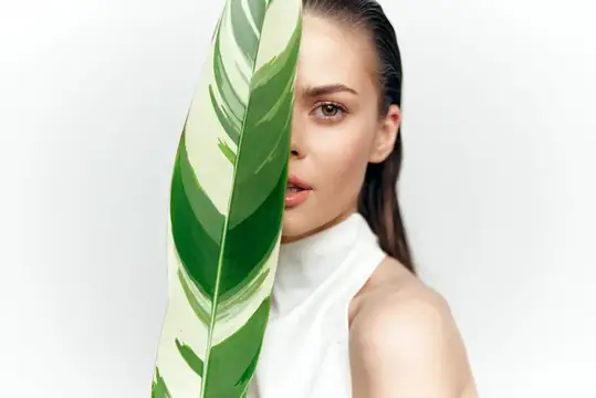 Молодая женщина с зелёным листом у лица на белом фоне