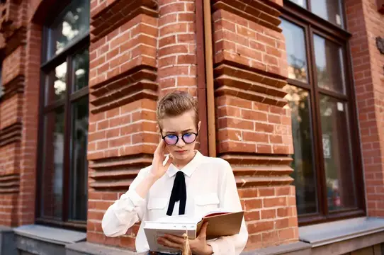 Молодая женщина в очках с блокнотом у кирпичного здания