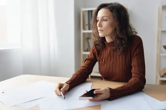 Задумчивая, серьезная, несчастная, милая кудрявая девушка сидит за столом с бумагами и документами, беспокоясь о проблемах на работе, размышляя о неудаче и банкротстве, рассчитывая бюджет и глядя в…