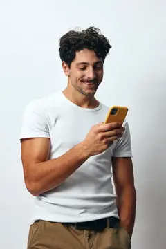 Кудрявый мужчина в белой футболке улыбается, глядя в смартфон