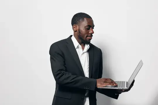 Темнокожий мужчина в деловом костюме работает за ноутбуком на светлом фоне
