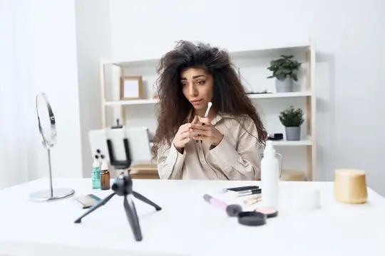 Кудрявая девушка записывает бьюти-видео на смартфон перед зеркалом