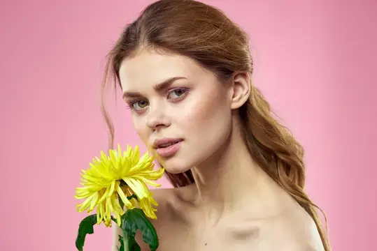 Красивая девушка с жёлтым цветком на розовом фоне, обнажённые плечи, макияж