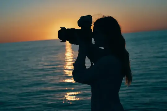 Силуэт девушки с фотокамерой на закате у моря