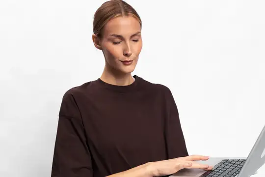 Сосредоточенная молодая женщина в темной кофте работает за ноутбуком на белом фоне