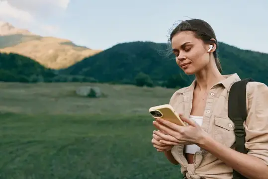 Девушка в наушниках смотрит в телефон на фоне гор