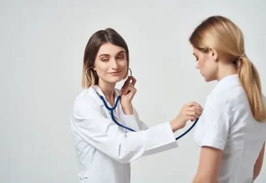 Женщина-врач в белом халате слушает пациентку стетоскопом
