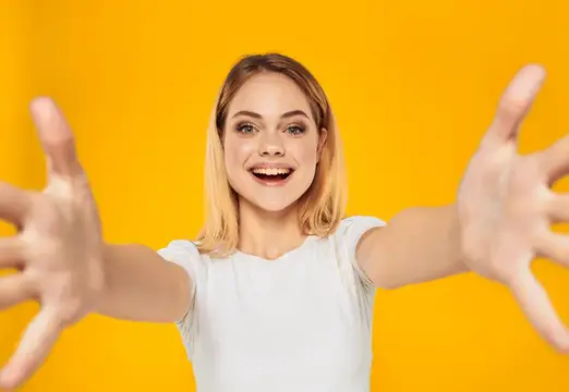 Улыбающаяся блондинка тянет руки к камере на жёлтом фоне