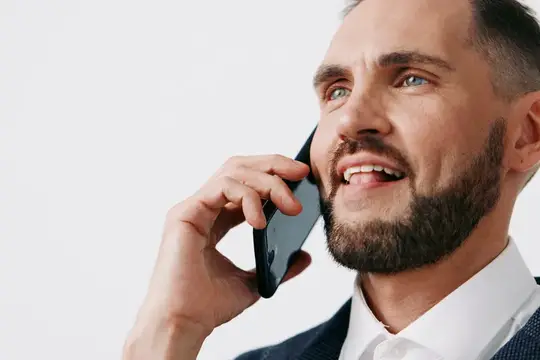 Улыбающийся бородатый мужчина говорит по телефону на белом фоне