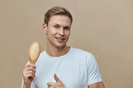 Улыбающийся светловолосый парень с массажной расчёской в руке