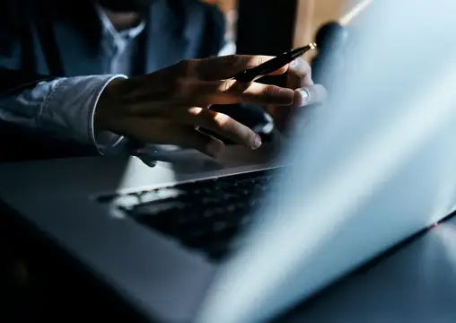 Мужчина в рубашке держит смартфон перед ноутбуком