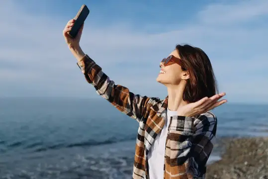 Женщина делает селфи на море, смартфон, на открытом воздухе, солнечный пляж, образ жизни, морской пейзаж у океана, приглашающая атмосфера путешествия и беззаботное настроение, запечатленные при…