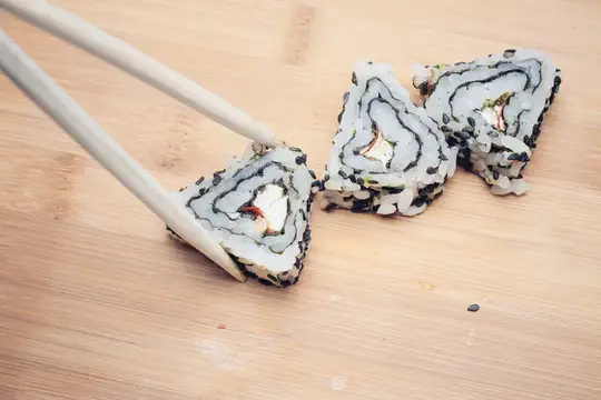 Палочки берут кусок ролла с лососем с деревянной доски