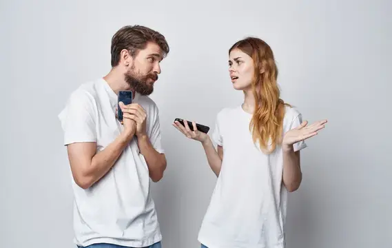 Рыжеволосая женщина с телефоном жестикулирует перед бородатым мужчиной