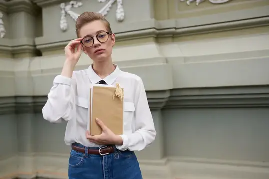 Молодая девушка в очках с книгой на фоне старинного здания