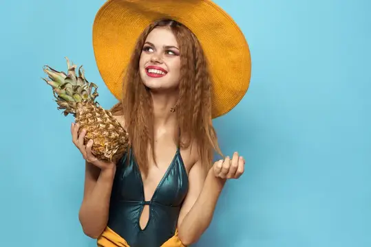 Улыбчивая девушка в жёлтой шляпе держит ананас на голубом фоне