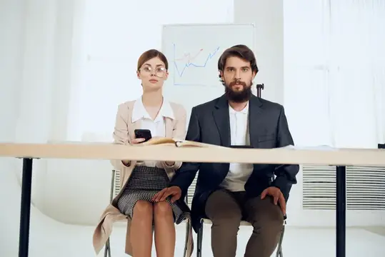Мужчина и женщина в деловых костюмах сидят за столом на фоне графика