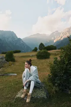 Молодая женщина сидит на камне в горах и смотрит вдаль