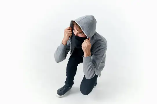 Мужчина в сером худи и чёрной маске сидит на корточках